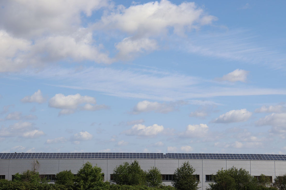 Groot bedrijfspand met een dak vol zonnepanelen, aangesloten op een zakelijke hybride omvormer voor energieopslag