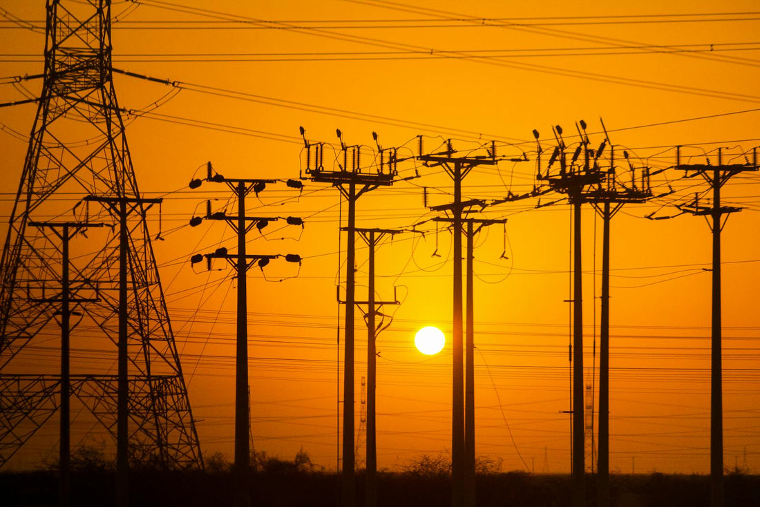 Hoogspanningsmasten in oranje avondzon, symbool voor de tijdsafhankelijke nettarieven die in 2029 voor huishoudens ingaan.