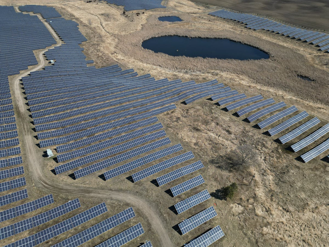 Luchtfoto van een groot zonnepark met rijen donkere zonnepanelen rond een vijver in landelijk gebied, illustratie bij Deye omvormer storingen en garantie 2026