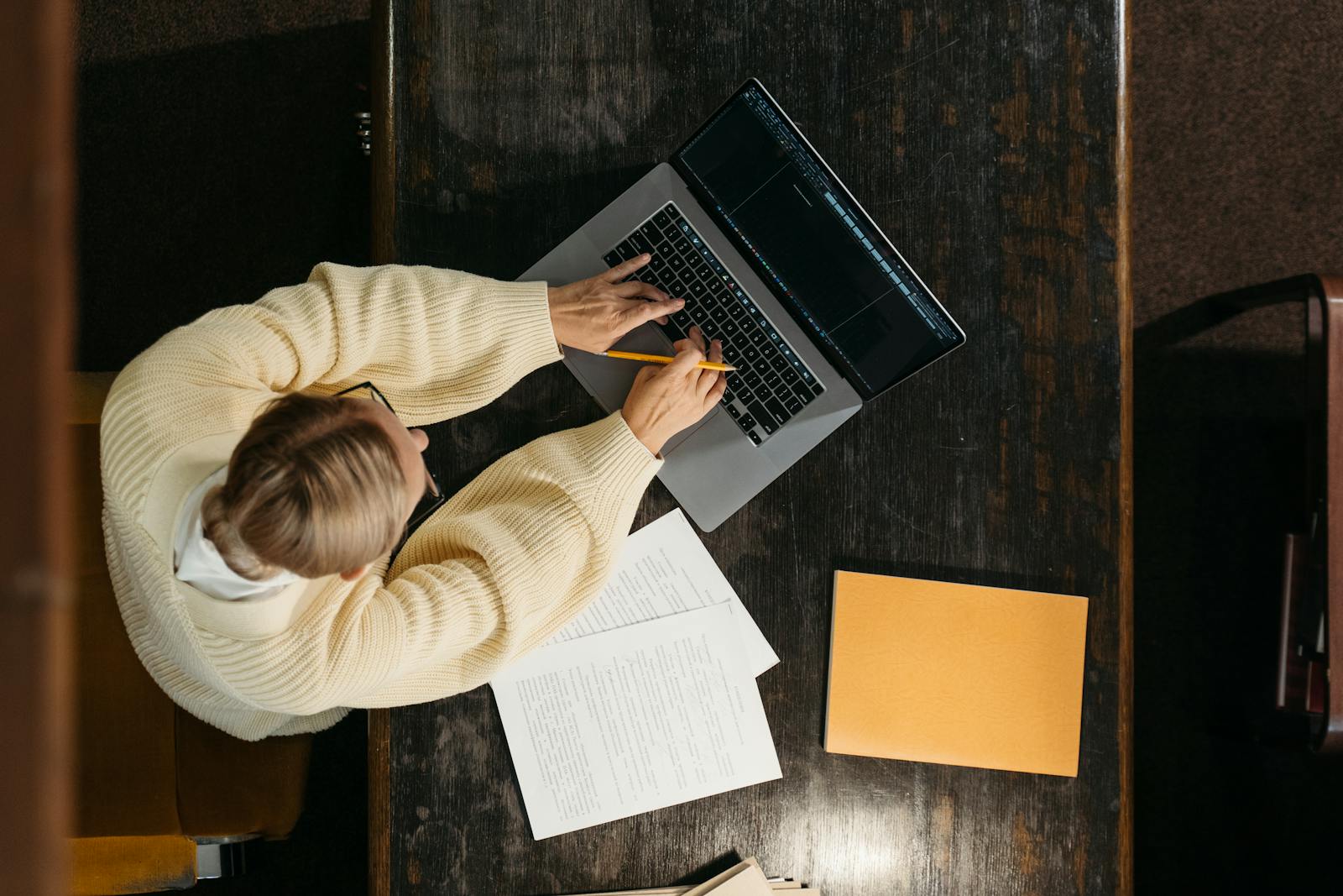 Persoon werkt aan een houten bureau aan administratie en formulieren op een laptop, passend bij de aanmelding van een thuisbatterij bij de netbeheerder