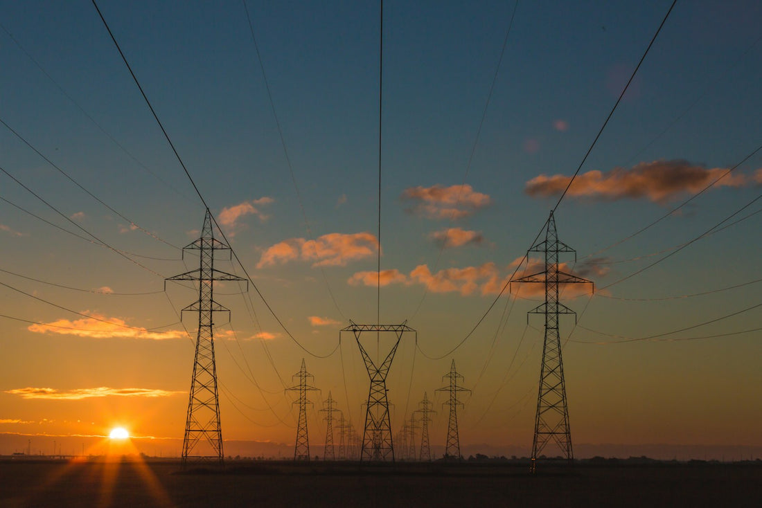 Hoogspanningsmasten in oranje avondzon symboliseren het Nederlandse stroomnet waar het capaciteitstarief 2026 voor kleinverbruik op aanstuurt.